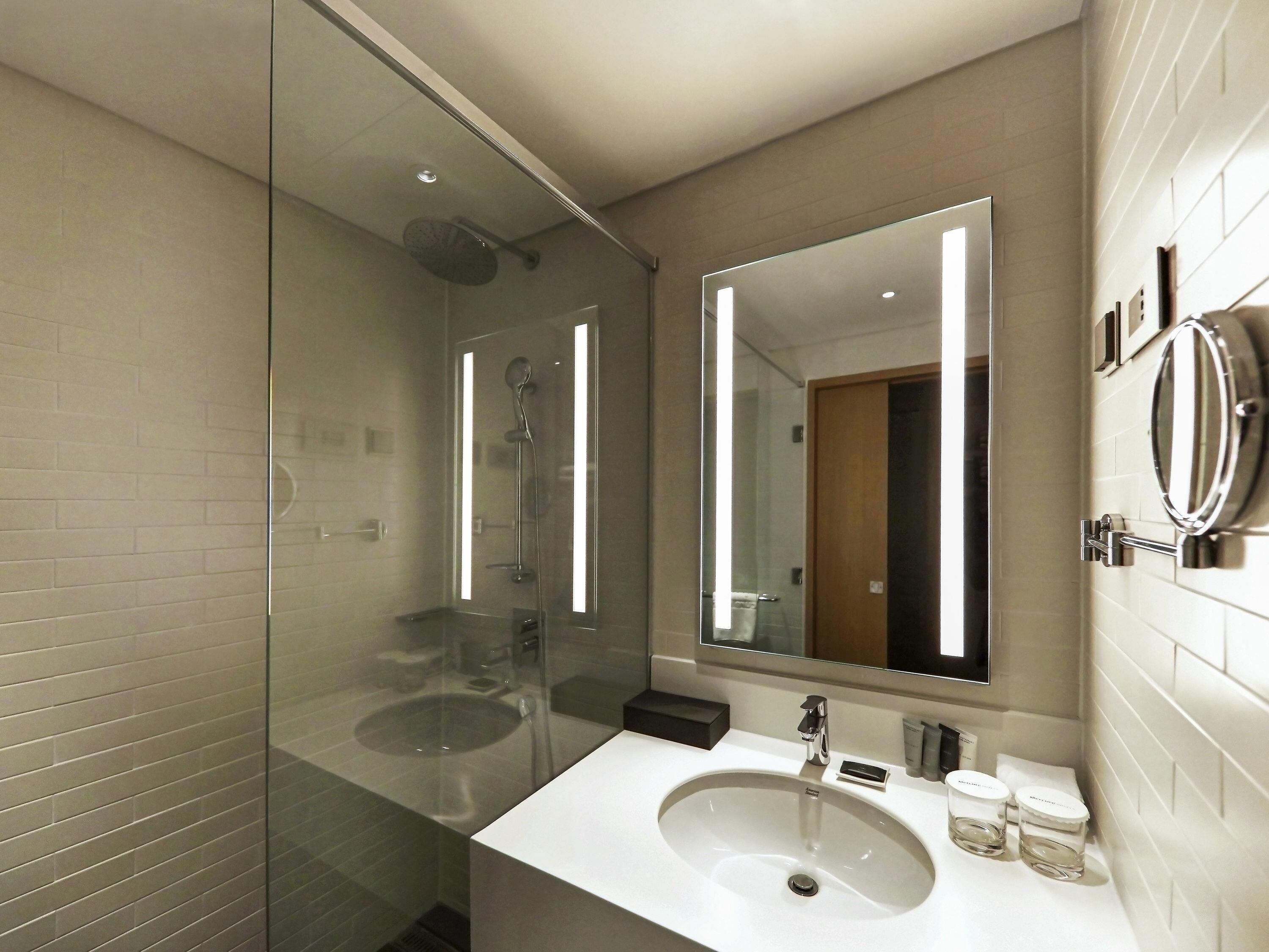 A modern bathroom with a glass-enclosed shower, a large mirror, and a white sink.