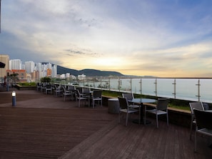 A wooden deck with outdoor seating, overlooking a body of water and a cityscape. - Mercure Ambassador Ulsan (Ulsan)