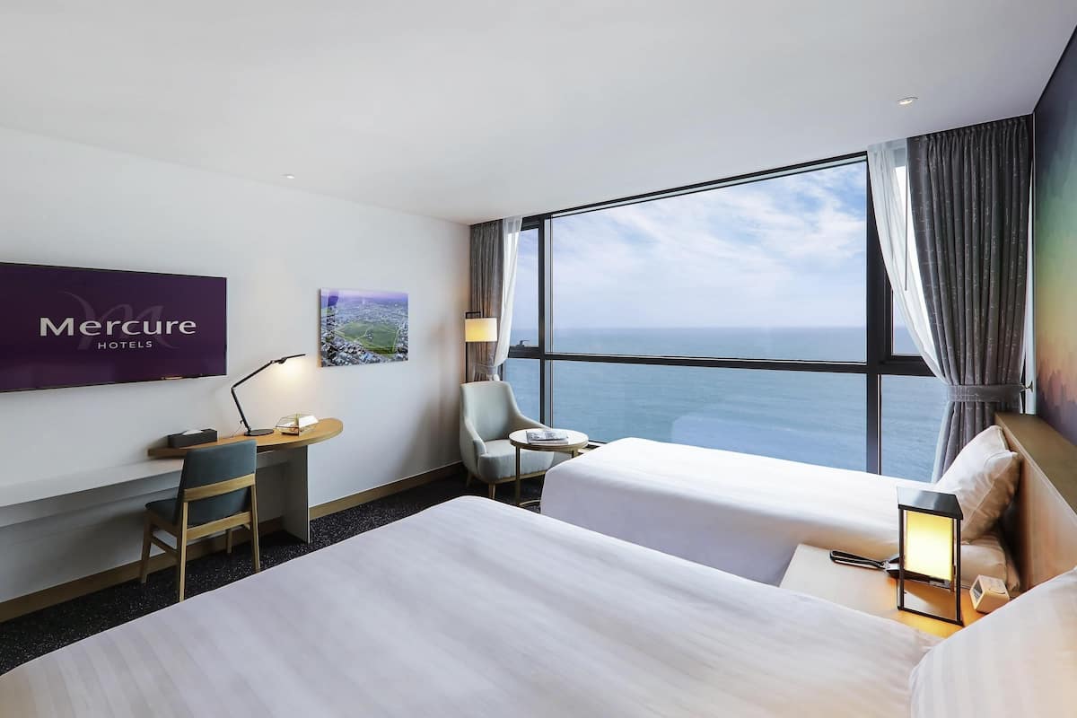 Una habitación de hotel con cama, escritorio, silla, televisor y ventana con vista al mar.