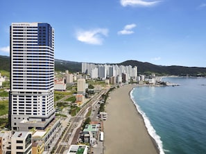 A coastal cityscape with a prominent hotel, a wide beach, and a mountain in the background. - Mercure Ambassador Ulsan (Ulsan)
