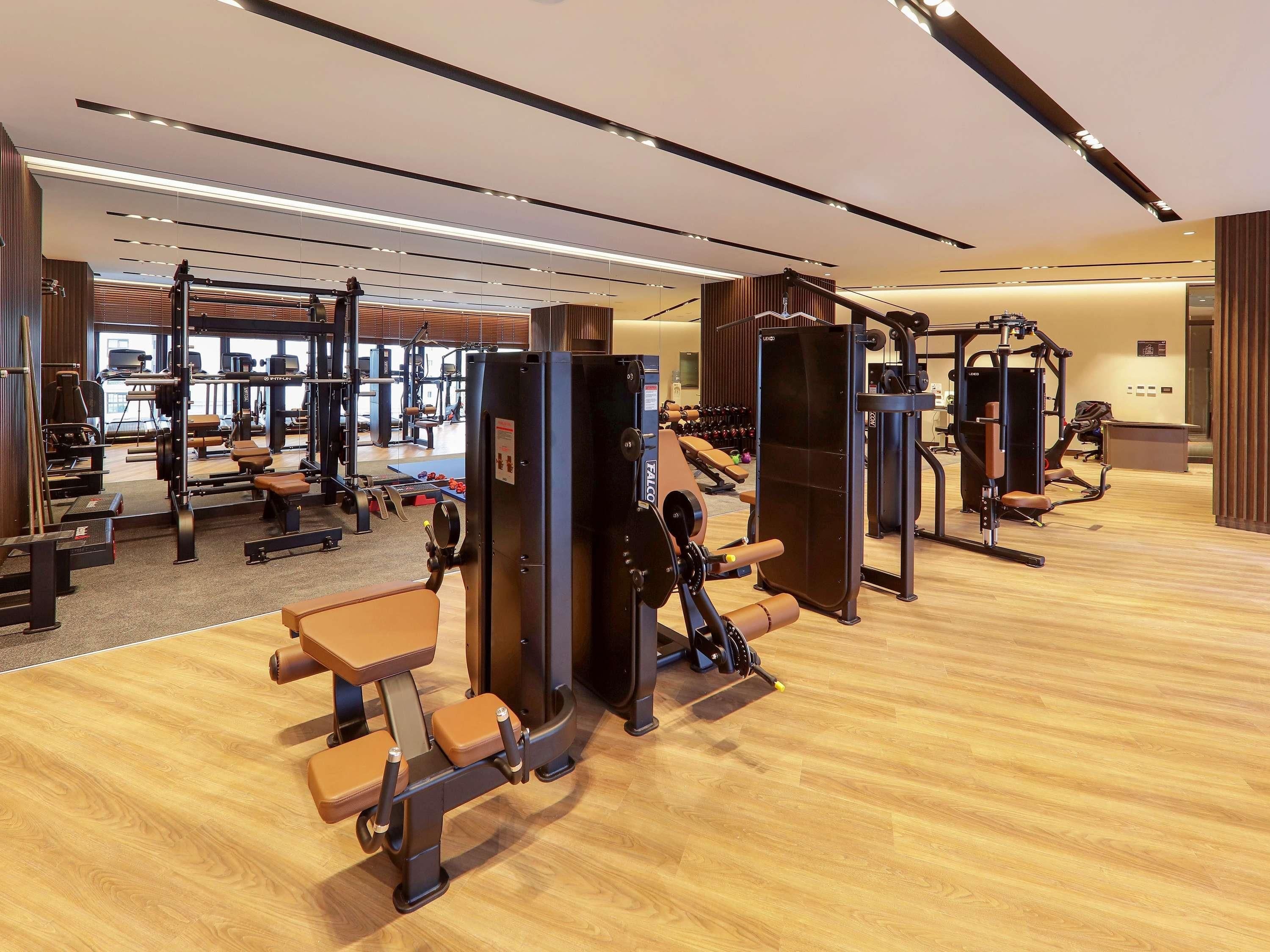 Et moderne fitnesscenter med forskellig træningsudstyr, trægulv og et lyst interiør.