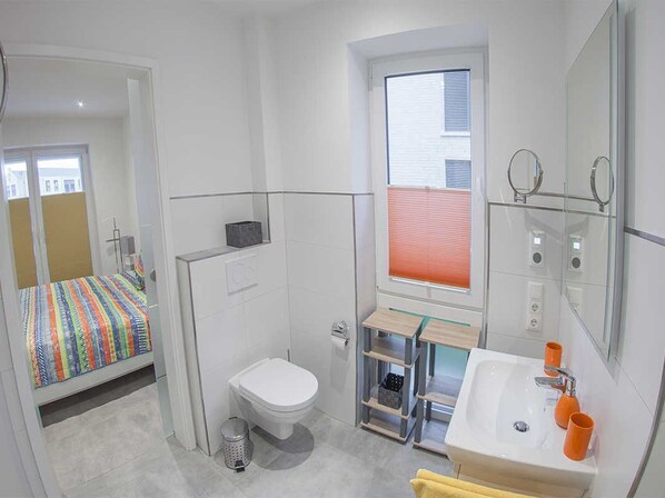 Een kleine hotelkamer met een bed, toilet, wastafel en een raam met jaloezieën.