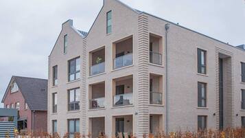 A modern multi-story residential building with balconies, a flat roof, and a brick facade.