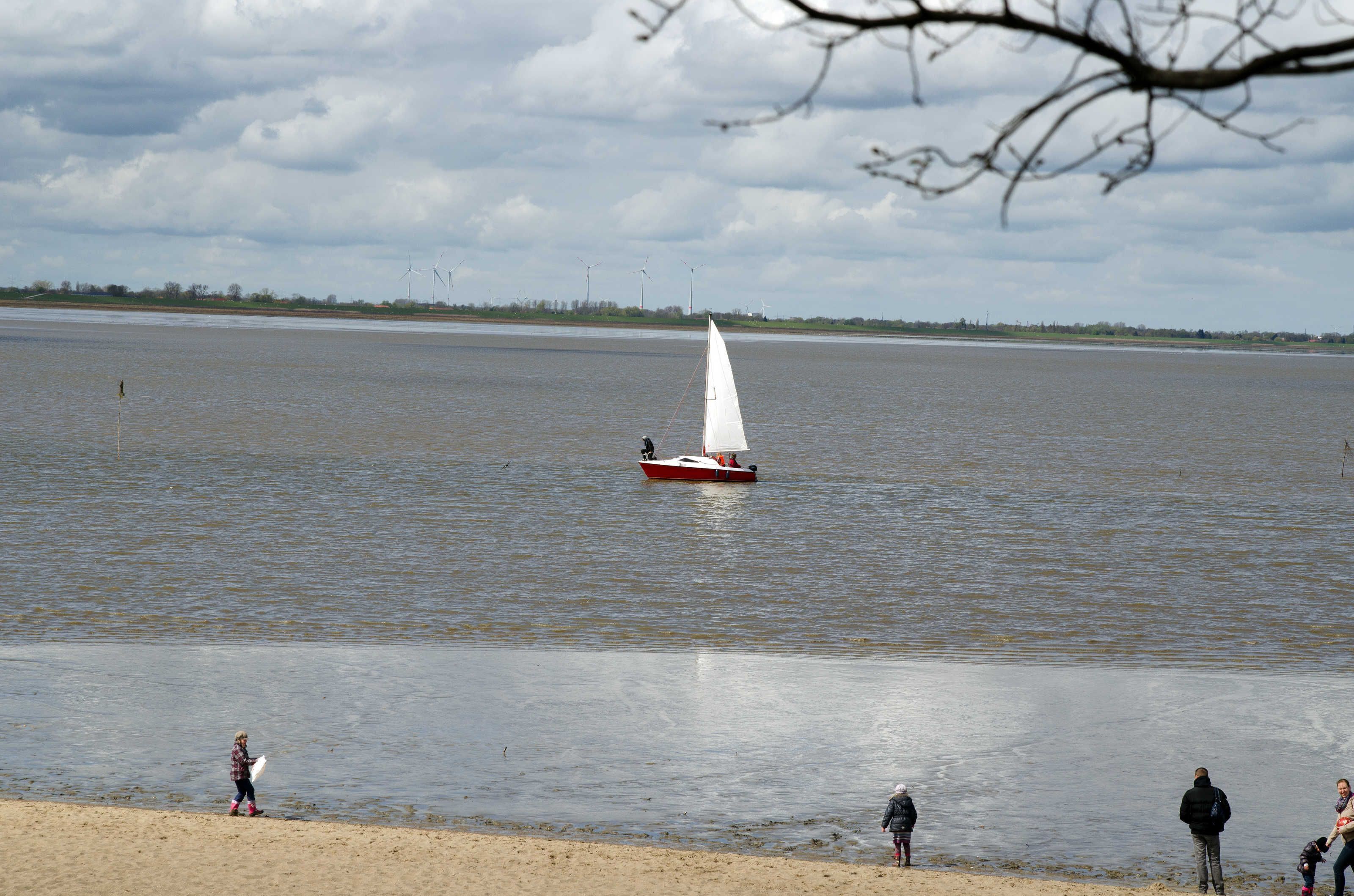 A calm lake with a sailboat and people on the shore.