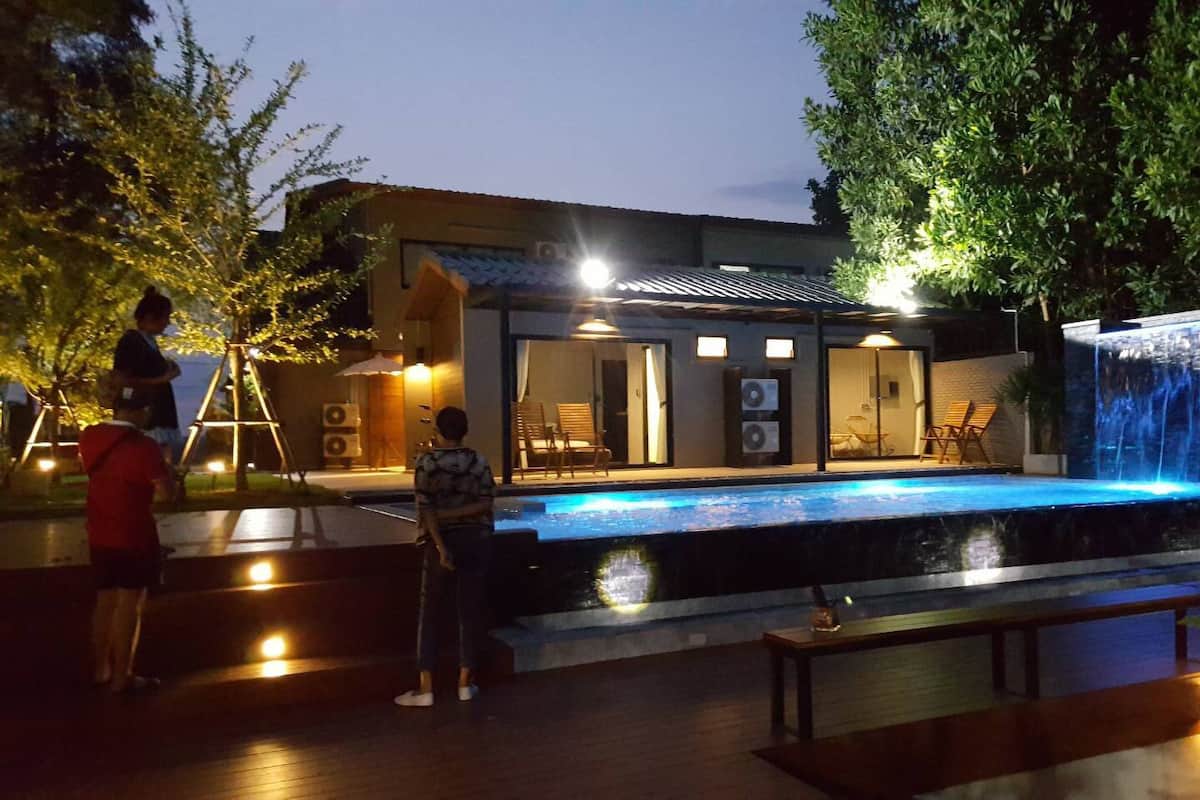 Une piscine extérieure agrémentée d’une cascade, entourée d’une terrasse en bois et d’un espace détente avec des sièges.