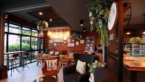 Un café chaleureux, avec des meubles en bois, de grandes fenêtres et un mur de briques orné d’œuvres d’art.