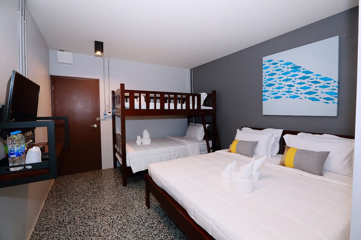 Une chambre d’hôtel avec deux lits, un lit superposé, un bureau avec une bouteille d’eau et un tableau au mur.
