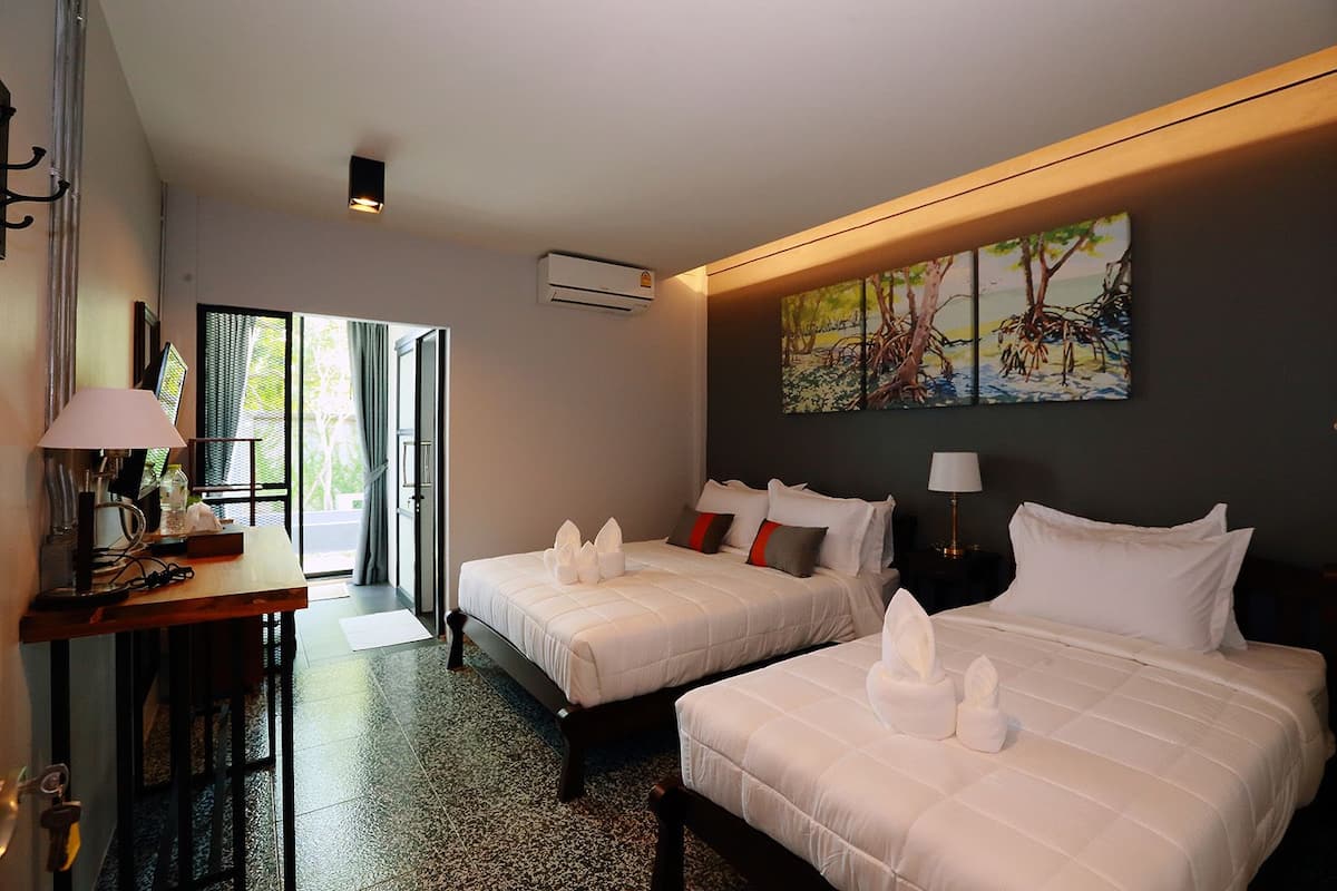 Une chambre d’hôtel avec deux lits, un bureau avec une lampe, un tableau au mur et un appareil de climatisation.