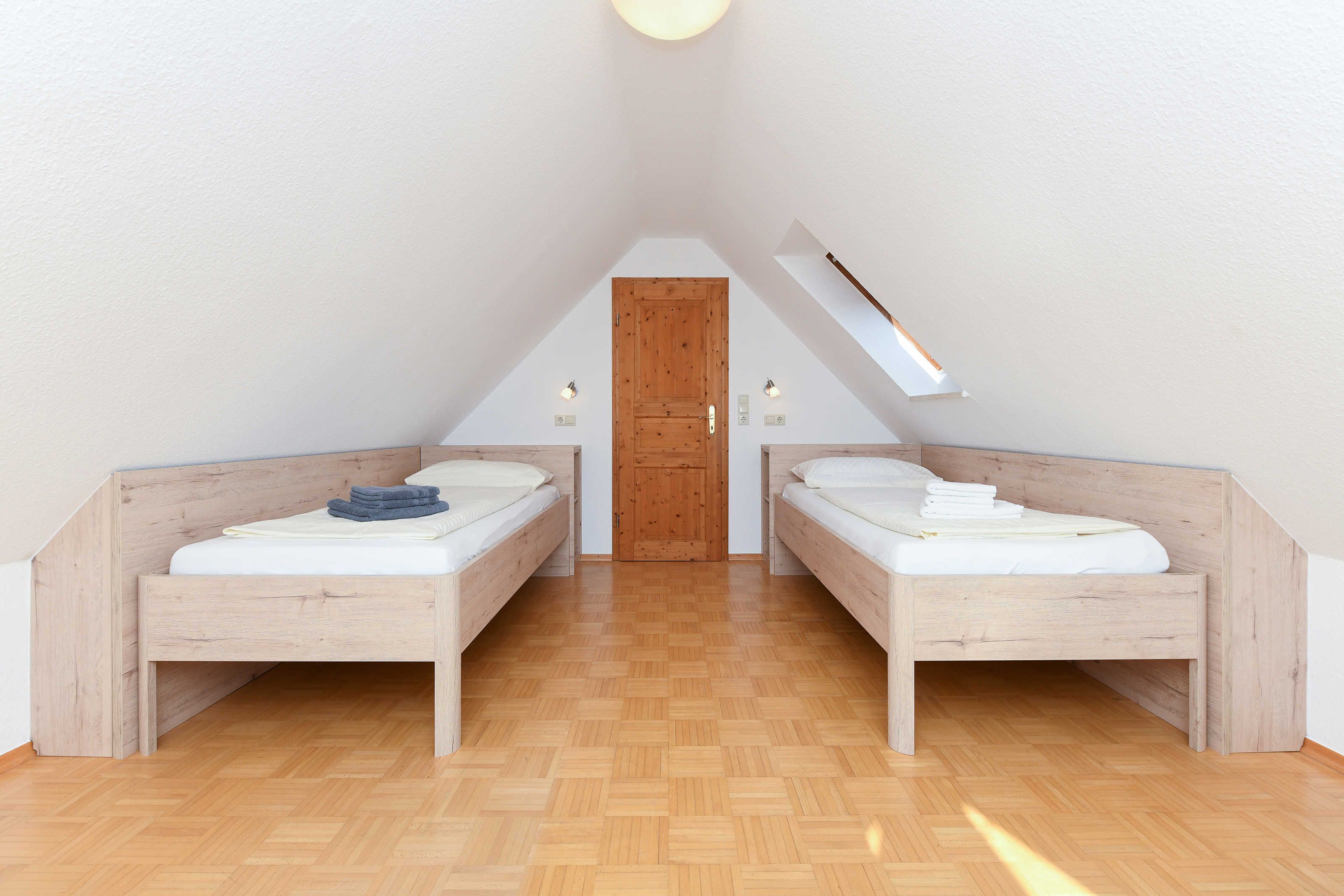 Una camera da letto con due letti in legno, una porta in legno e un soffitto spiovente con finestra a lucernario.