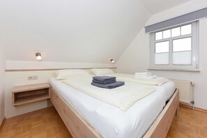 Et soveværelse med seng, sengeborde, et vindue med persienner og en radiator.