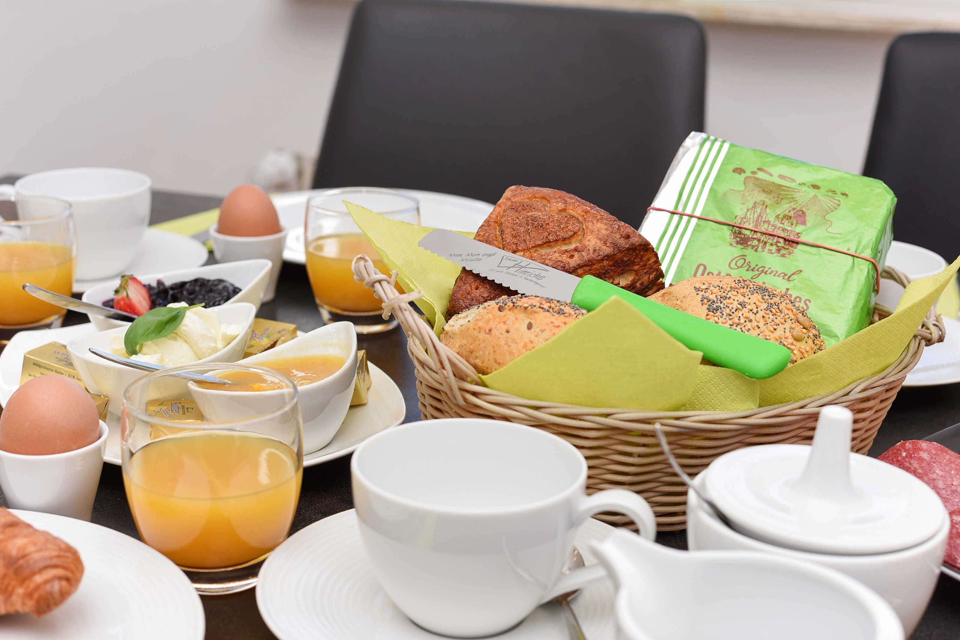 A breakfast setting with a wicker basket containing bread, a knife, and a packet of butter.