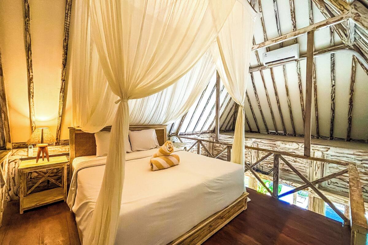 A bedroom with a canopy bed, wooden flooring, and a view of the outdoors.
