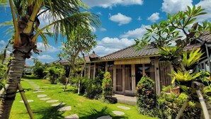 A tropical resort with a well-maintained lawn, stone pathways, and traditional wooden structures.