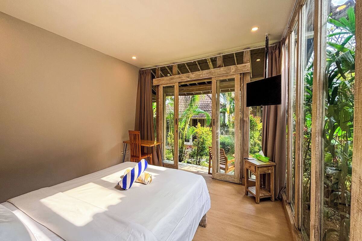 A bedroom with a bed, a TV, and a view of a garden.