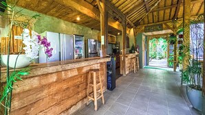 A rustic kitchen with wooden beams, a bar area with stools, and a view of the outdoor garden.