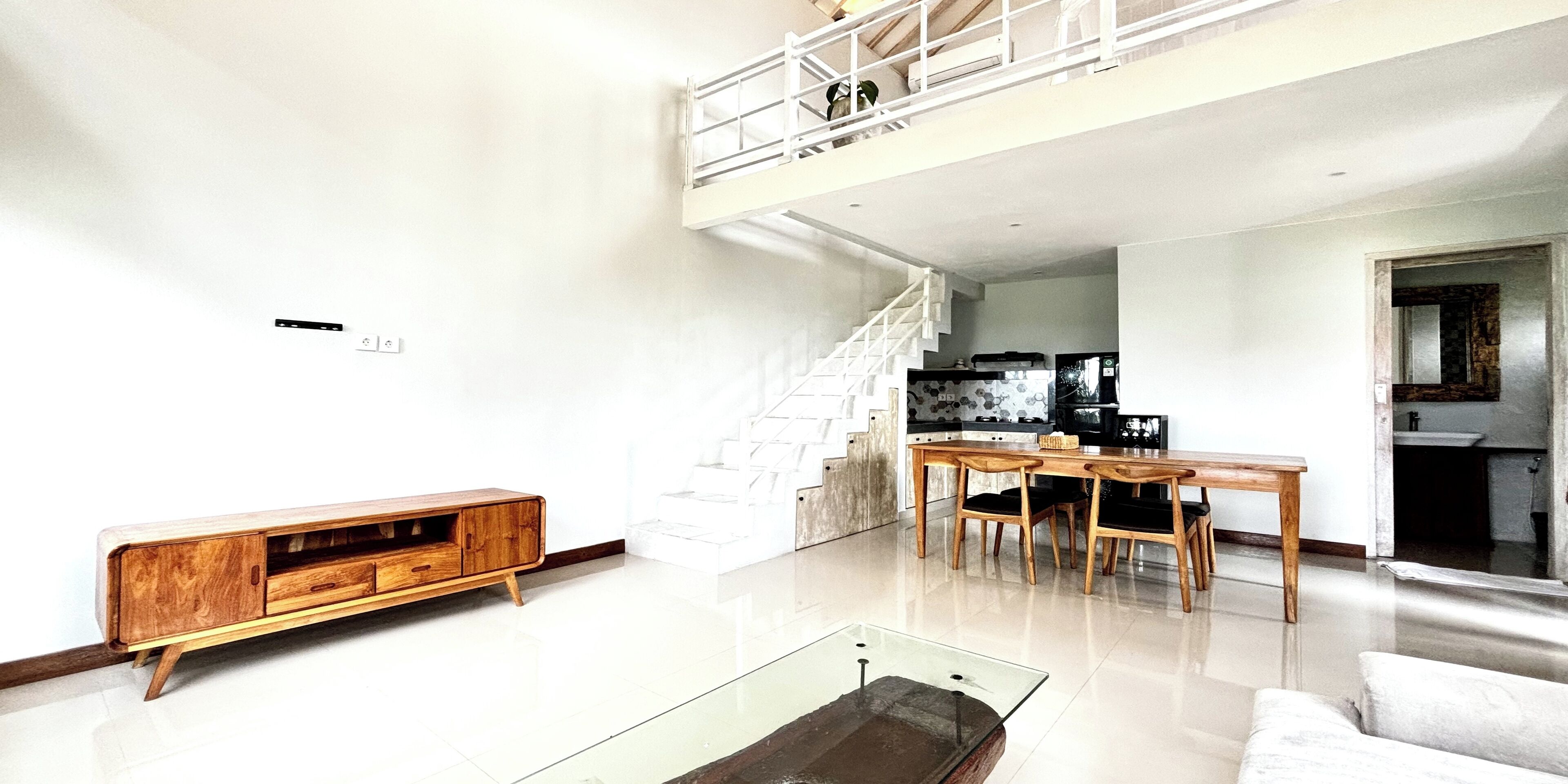 A spacious living area with a wooden console, a glass coffee table, and a staircase leading to an upper level.