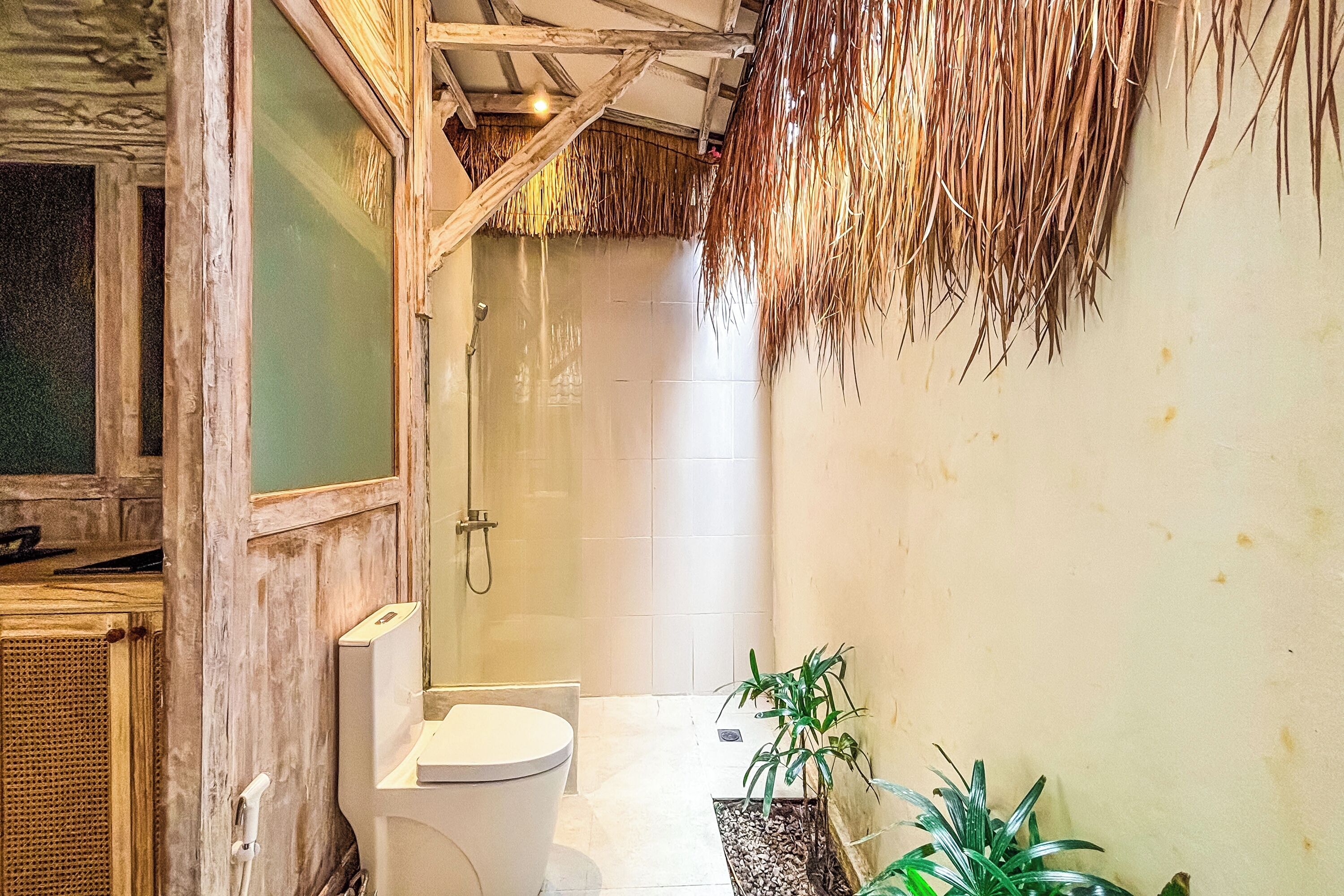 A bathroom with a rustic design, featuring a wooden door, a white toilet, a shower area, and a small potted plant.