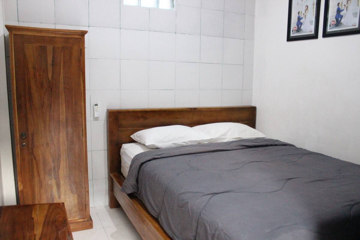 A bedroom with a wooden wardrobe, a bed with white and gray bedding, and a tiled wall.