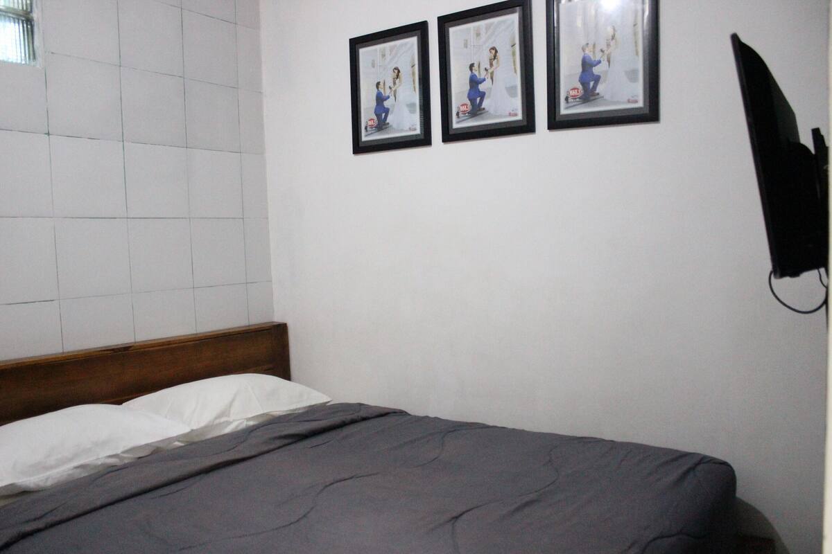 A bedroom with a bed, a wooden headboard, and three framed pictures on the wall.