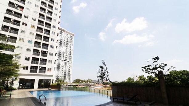 A swimming pool surrounded by a tiled patio area, with a tall residential building in the background.