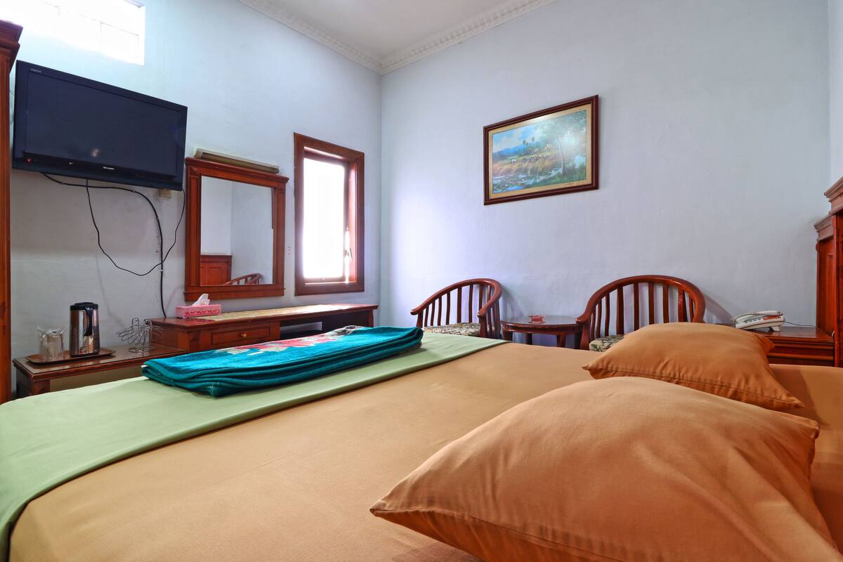 A hotel room with a bed, a desk, a chair, a television, a painting, and a window.