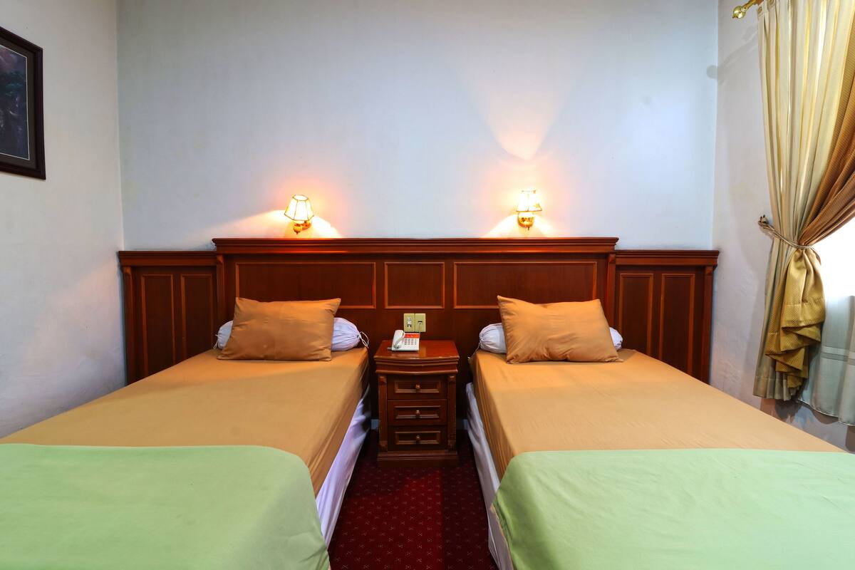A hotel room with two single beds, a wooden nightstand with a telephone, and wall-mounted lamps.