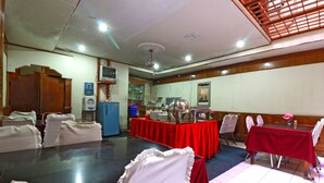 A conference room with a large table, white chairs, and red tablecloths. There are kitchen appliances and a water dispenser in the background. - Hotel Sumatera (Medan)