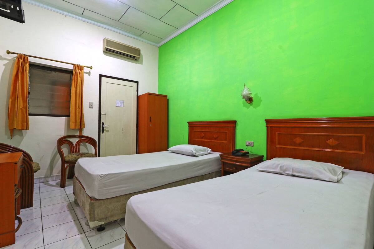 A room with two beds, a chair, a wardrobe, and a green wall.
