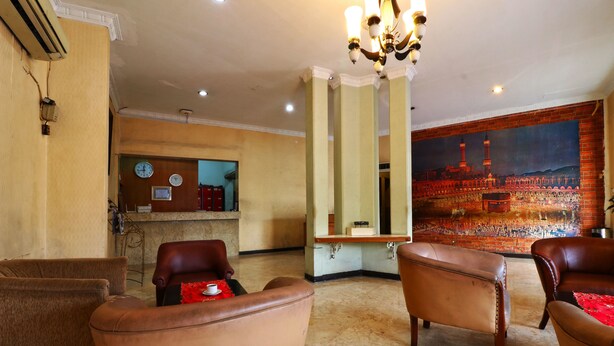 A lobby with leather armchairs, a reception desk, a large mirror, and a mural of a cityscape. - Hotel Sumatera (Medan)