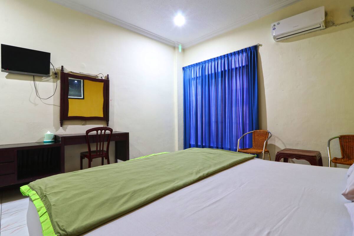 A hotel room with a bed, a desk, a chair, a television, and an air conditioning unit.