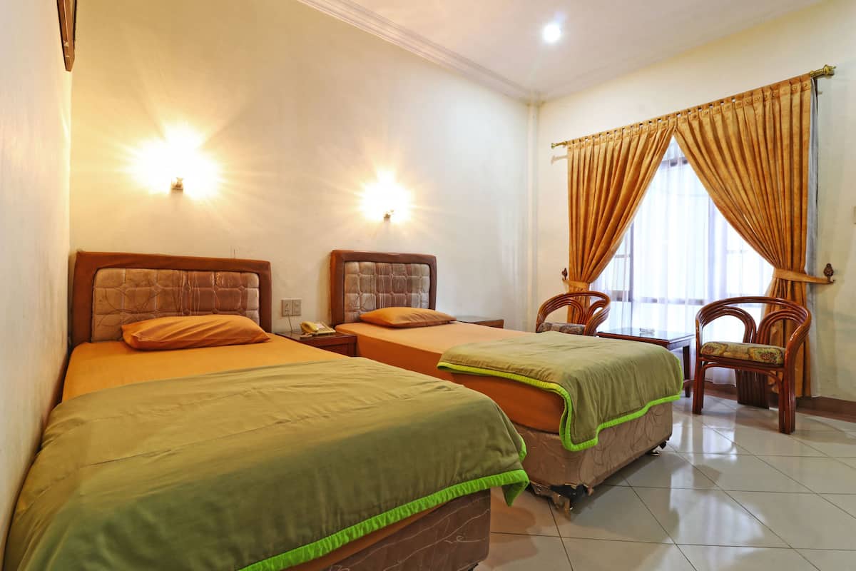 A hotel room with two beds, a wooden headboard, a nightstand, a chair, and a window with curtains.