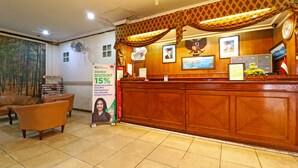 A hotel reception area with a wooden reception desk, a fan, and a poster advertising a 15% discount. - Hotel Melati (Medan)