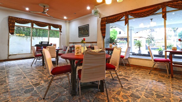 A dining area with stone flooring, red chairs, a central table, and large windows with curtains. - Hotel Melati (Medan)