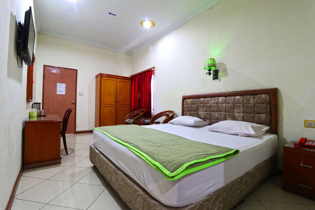 A hotel room with a bed, a desk, a chair, a wardrobe, a television, and a telephone.