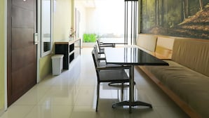A modern living room with a sofa, a dining table, and chairs. There is a door on the left and a window on the right. - Home Guesthouse by Zuzu (Surabaya)