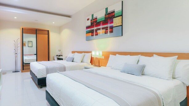 A hotel room with two beds, a desk, a chair, a mirror, and a colorful abstract painting on the wall. - Home Guesthouse by Zuzu (Surabaya)
