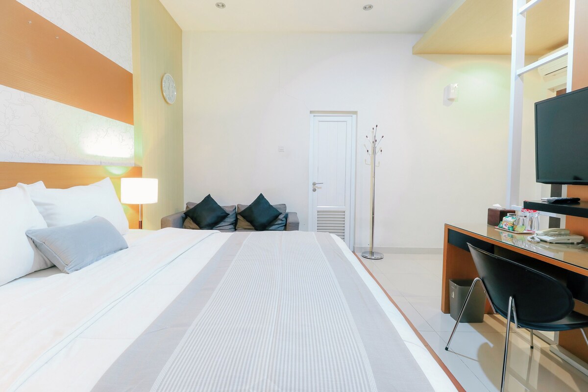Habitación de hotel con cama, escritorio, silla, televisor y puerta.