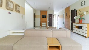 A modern living room with a sectional sofa, a glass coffee table, and a television mounted on the wall. - Home Guesthouse by Zuzu (Surabaya)