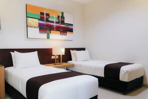 Habitación de hotel con dos camas, una mesita de noche con lámpara y un cuadro abstracto colorido en la pared.