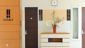 A hotel reception area with a wooden door, a white reception desk, a clock, and a flower vase. - Home Guesthouse by Zuzu (Surabaya)