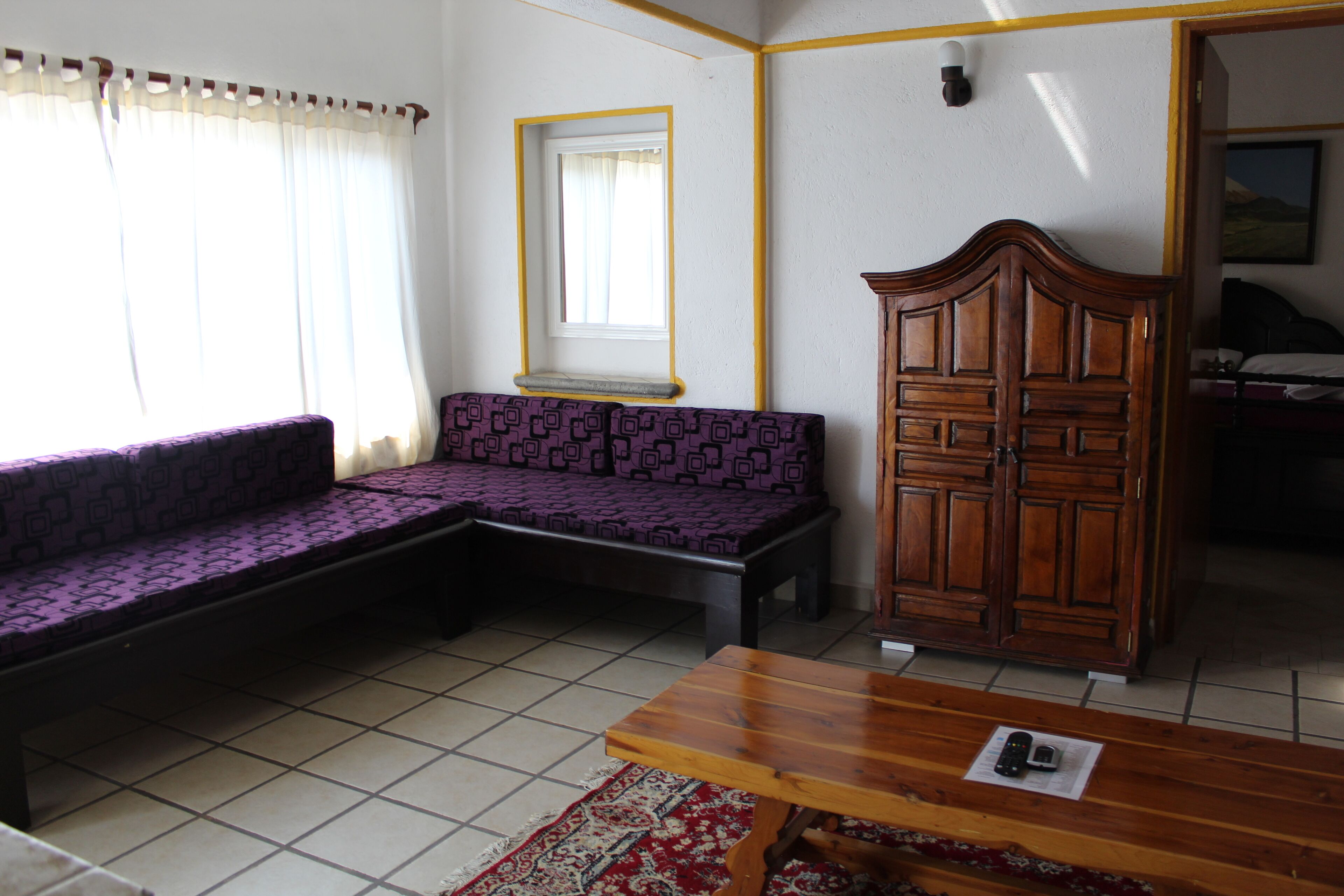 Une pièce avec un canapé à motifs violets, un meuble en bois et une petite table sur laquelle se trouve une télécommande.