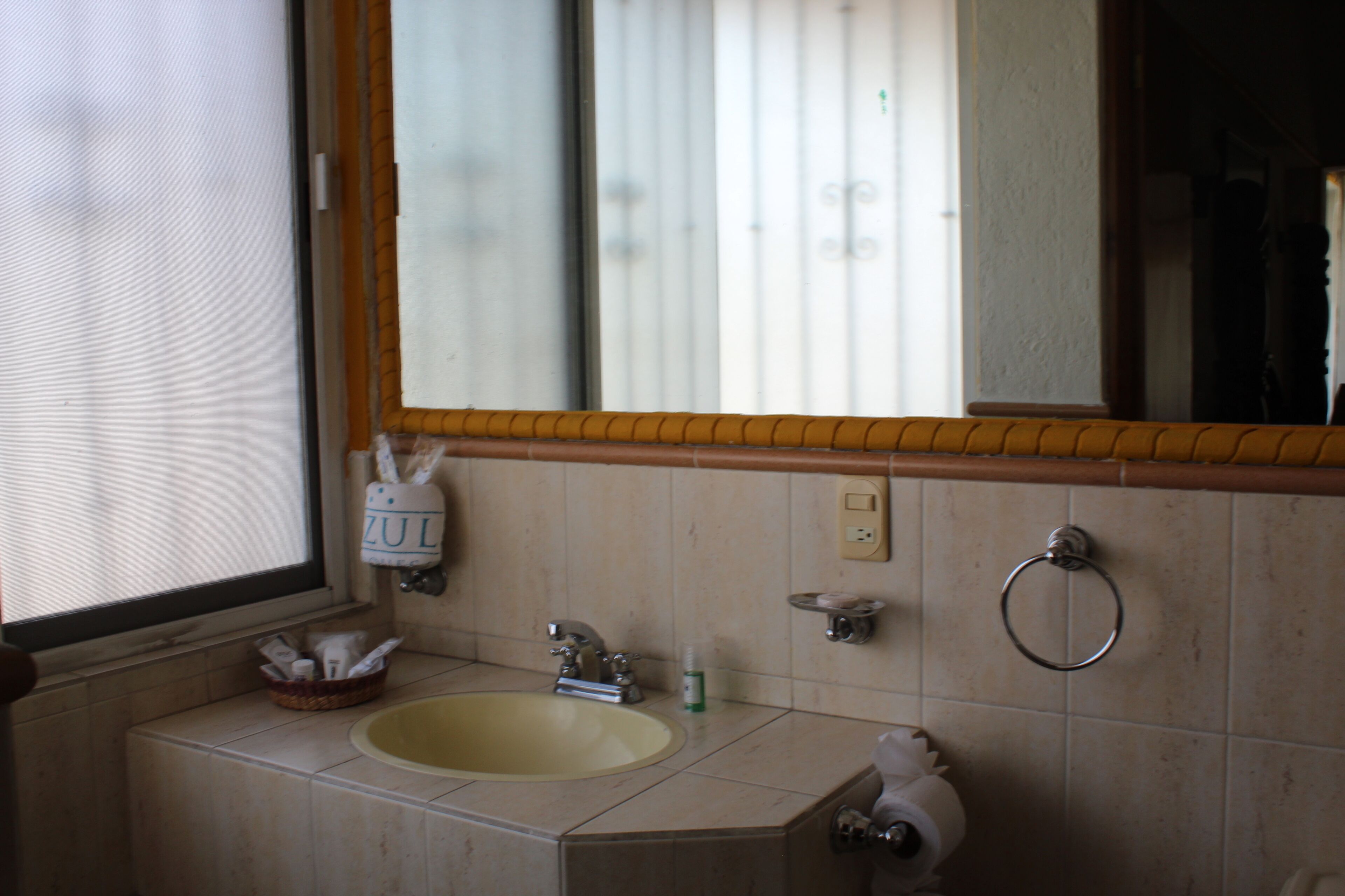 Un baño con lavamanos, espejo, toallero y ventana.