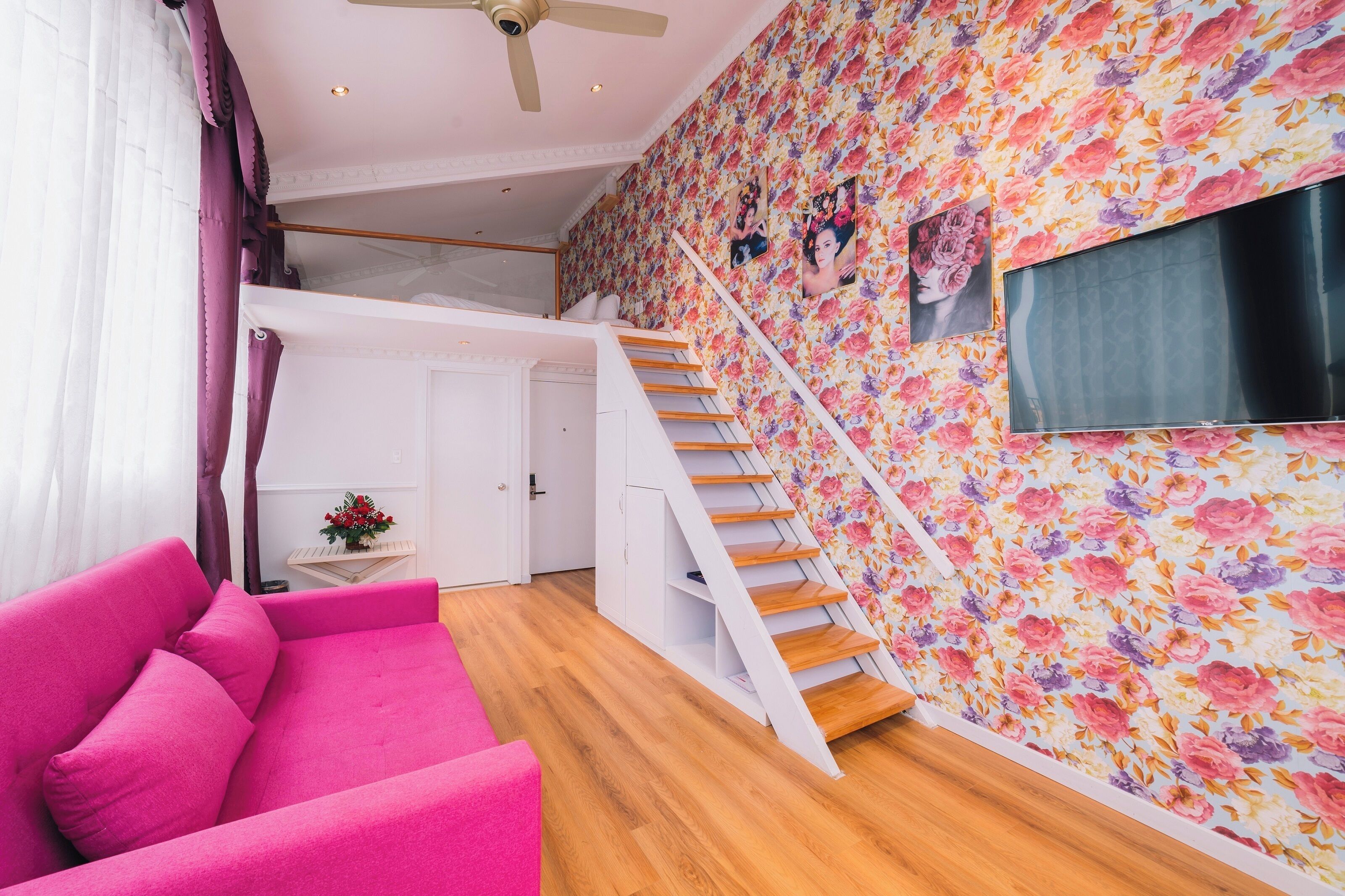 A modern interior with a pink sofa, wooden staircase, and a floral wallpaper.