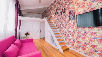 A modern interior with a pink sofa, wooden staircase, and a floral wallpaper.