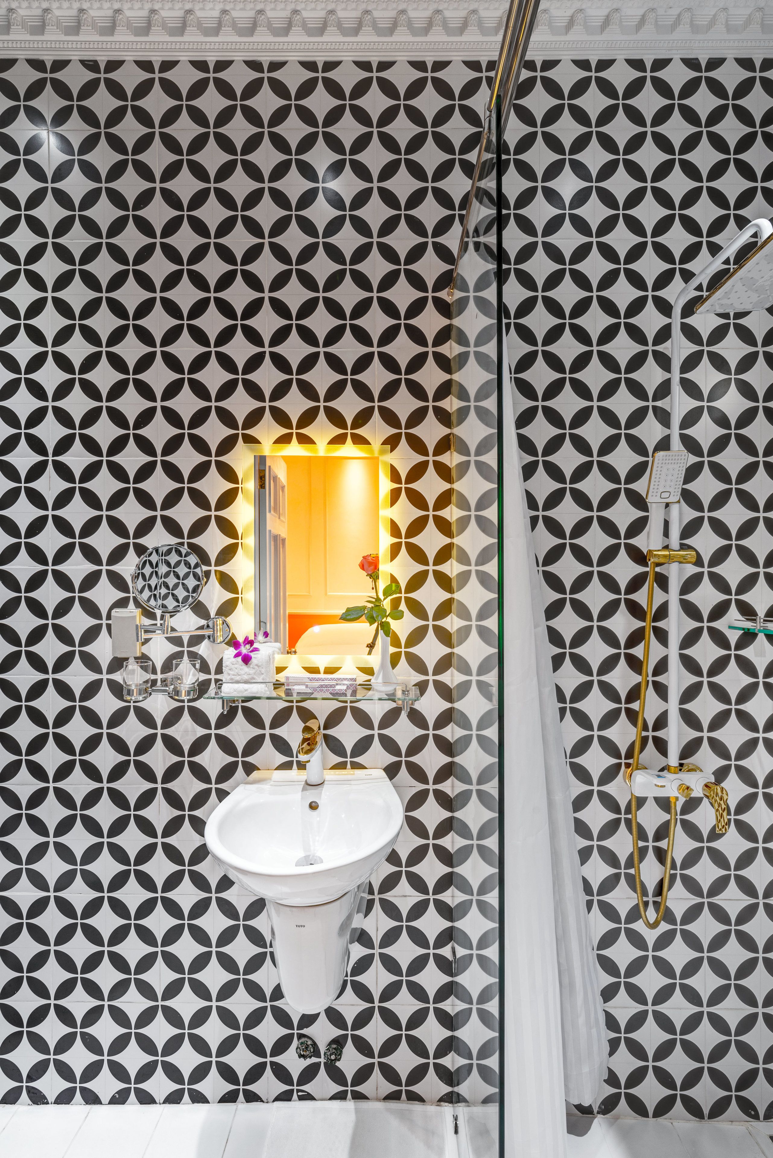 A bathroom with a geometric patterned wall, a pedestal sink, a mirror, and a shower area.