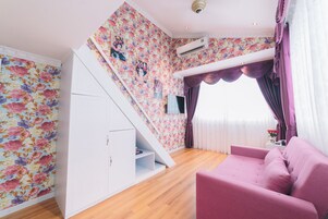Una habitación con piso de madera, un sofá rosa, un armario blanco y una escalera con papel tapiz floral.
