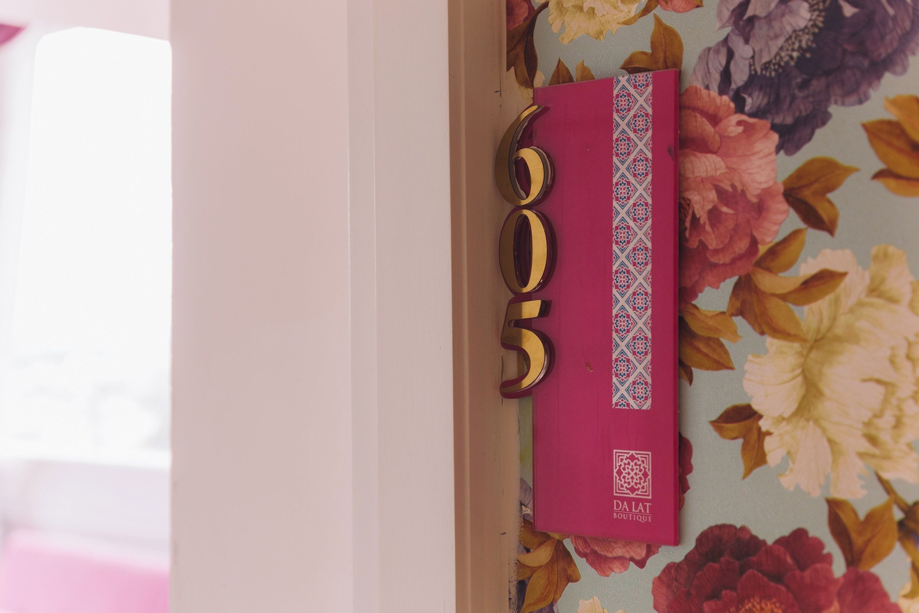 A door with a floral wallpaper background and a pink and gold decorative element.