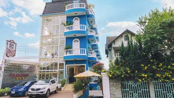 Een boutique hotel in blauw en wit met een glazen gevel, een balkon met planten en een klein terras.