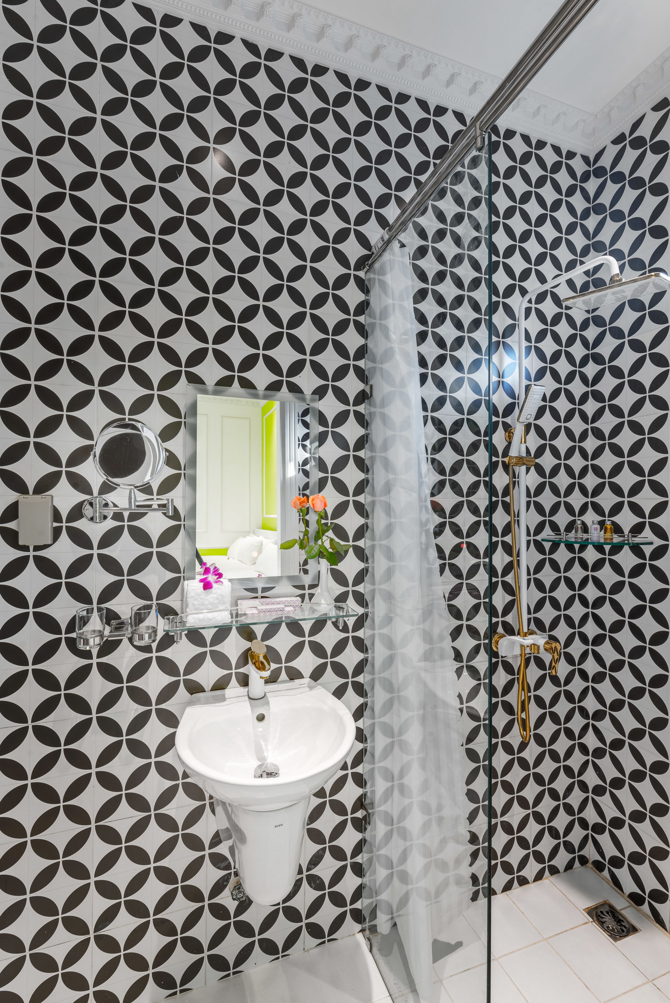 A bathroom with a geometric patterned wall, a white sink, a mirror, and a glass-enclosed shower area.