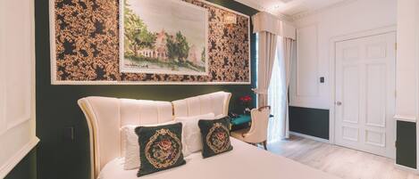 A bedroom with a large bed, a framed landscape painting, and a chandelier.